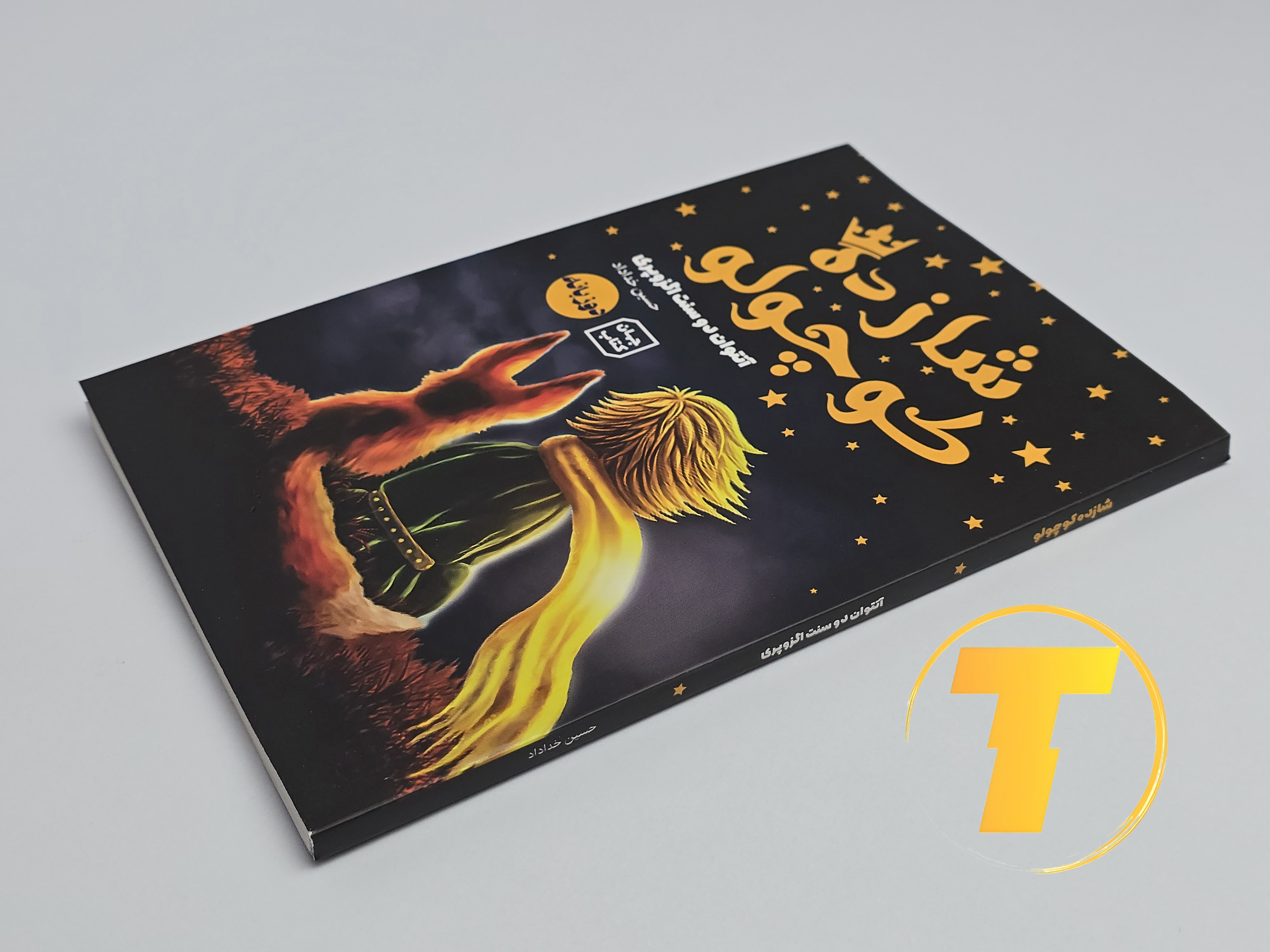 تاب شازده کوچولو روی میز سفید – تصویری از جلد و کناره‌های کتاب چاپ‌شده توسط نشر آثار نور