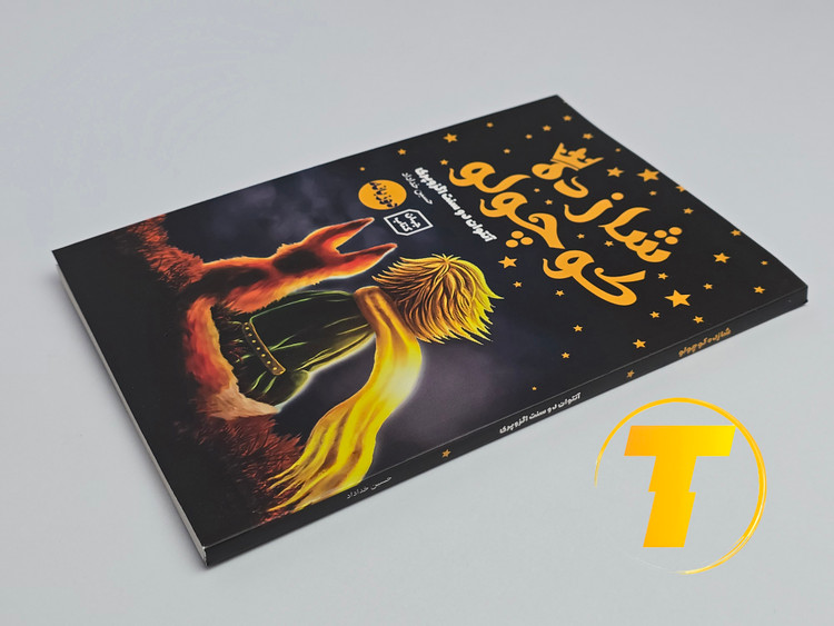 تاب شازده کوچولو روی میز سفید – تصویری از جلد و کنارههای کتاب چاپشده توسط نشر آثار نور