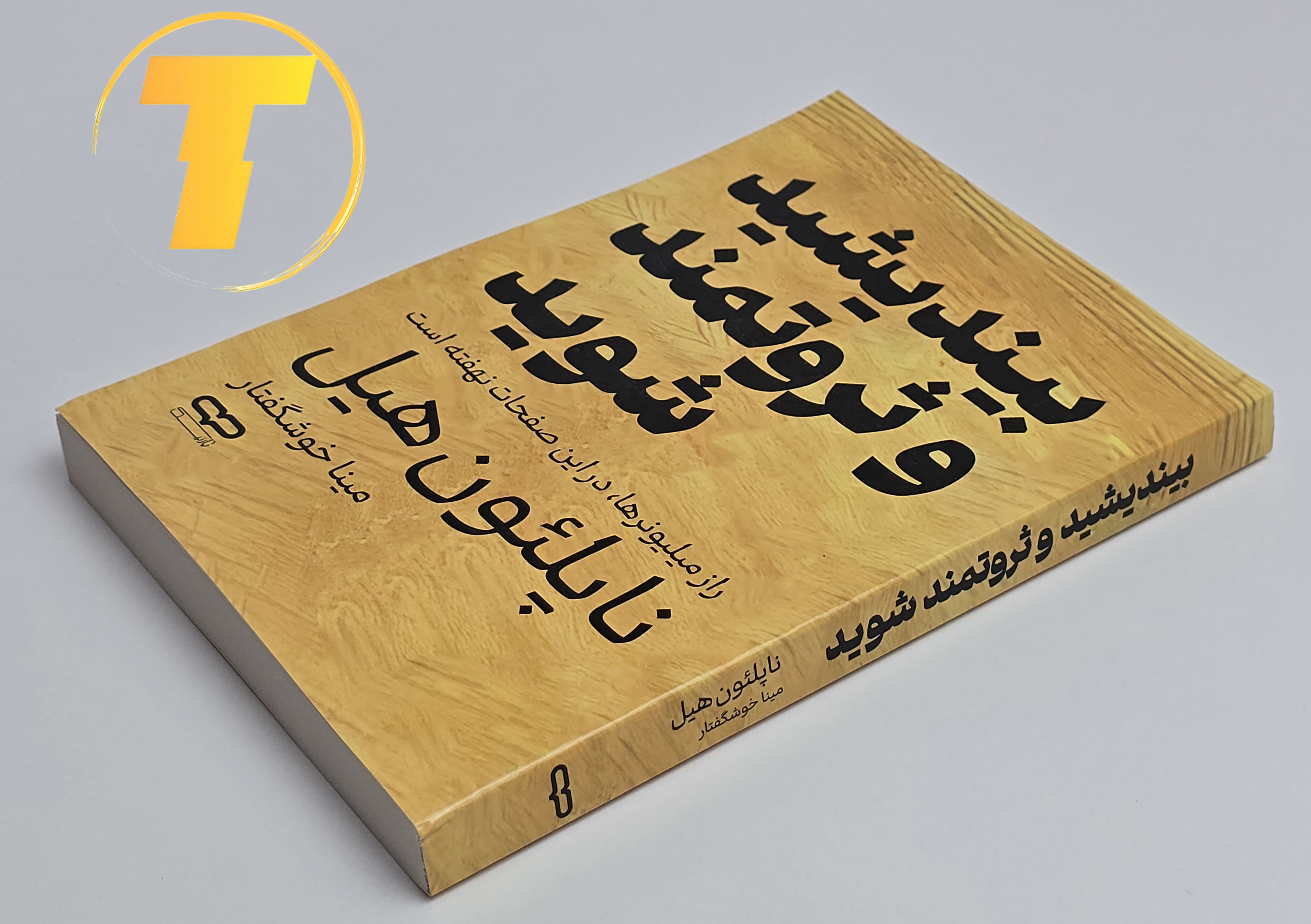 کتاب بیندیشید و ثروتمند شوید روی میز سفید – تصویری از جلد و کناره‌های کتاب چاپ‌شده توسط نشر یارنیک