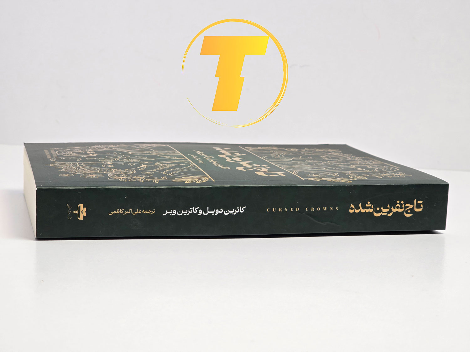 کتاب تاج نفرین شده با جلد شومیز روی میز مطالعه